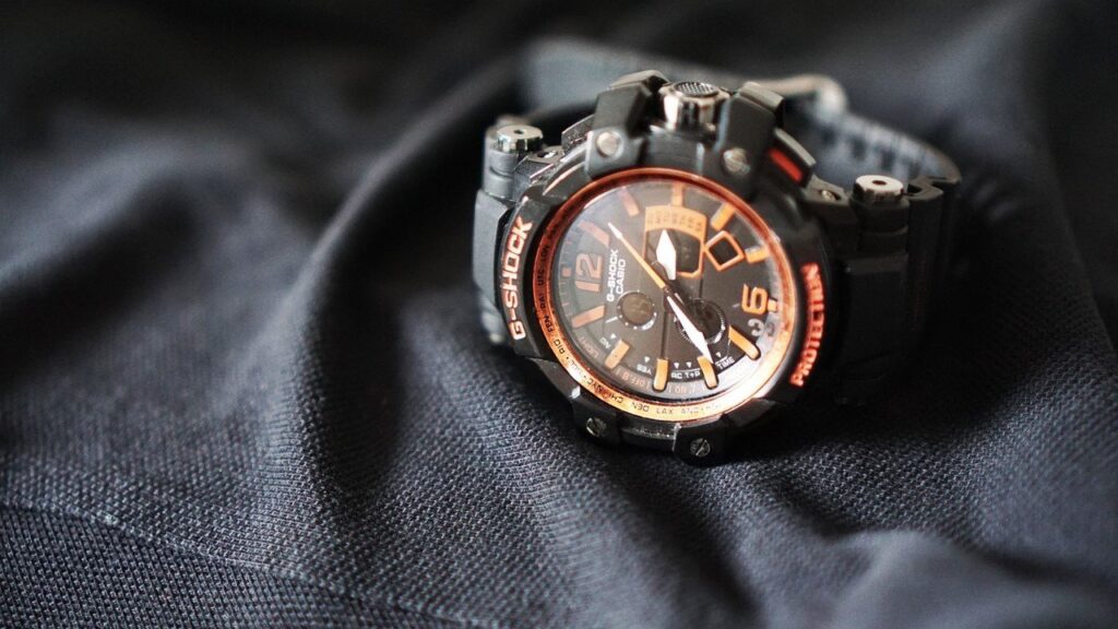 Reloj analógico Casio G-Shock negro y naranja sobre fondo de tela negra.